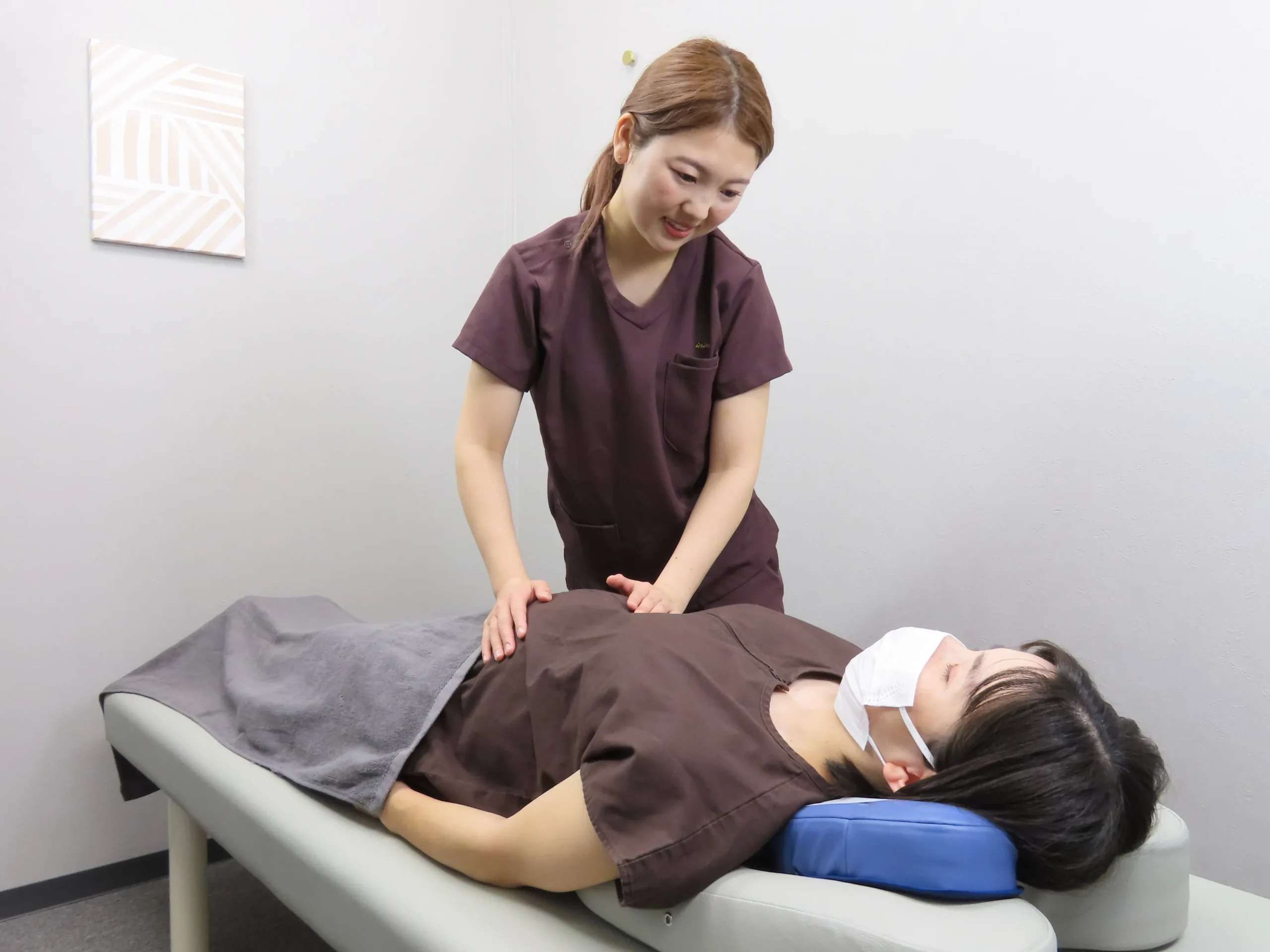 女性施術者がベッド上で患者のお腹に手を添えながらやさしく整体を行っている様子。自律神経や内臓調整に対応した施術の写真。